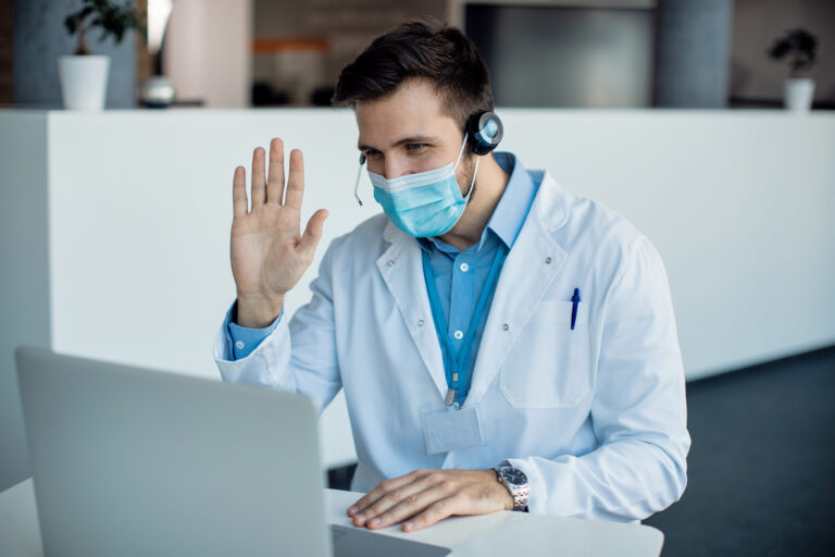 Male doctor waving during a video call over laptop at medical c